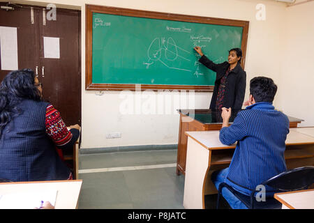 A young beautiful lady professor teaching and explaining science subject topic respiration by drawing diagram using chalk on chalkboard. Stock Photo