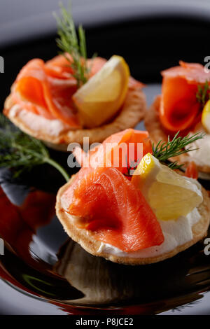 Tartlets with salmon , cream and a slice of lemon on a black plate. Stock Photo