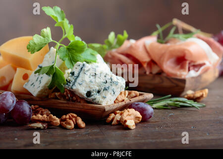 Various cheeses , grapes and prosciutto on a old wooden table. Stock Photo