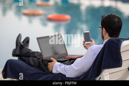 middle aged arab man working during his summer holiday by a pool Stock Photo