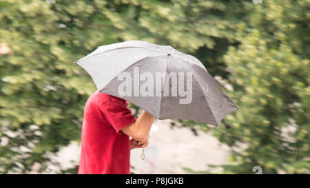 Blurry panning shot of a  man walking under umbrella in the spring rain in the city park Stock Photo