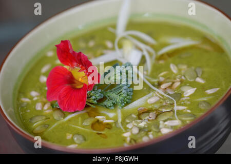 A bowl of healthy Green Goddess home-made soup made of freshly pureed organic greens and vegetables decorated with Nasturtium and pumpkin seeds Stock Photo