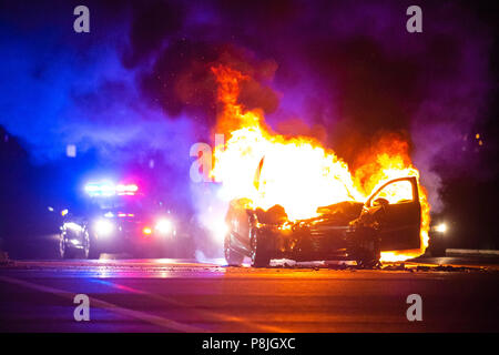 Car on fire at night with police lights in background noone Stock Photo
