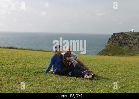 Father beautiful mother and daughter family cuddle with sea in background in Cornwall Stock Photo