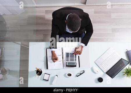 Happy African Businessman Looking At Laptop Calculating Invoice In The Office Stock Photo
