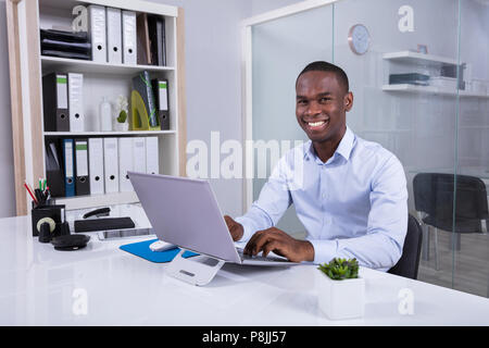 Portrait Of Smiling Young Businessman Using Laptop At Workplace Stock Photo