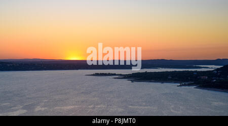 The sun sets in a blaze of brilliant orange, pink, and yellow over Lake Travis in the hill country of central Texas near Austin. Stock Photo