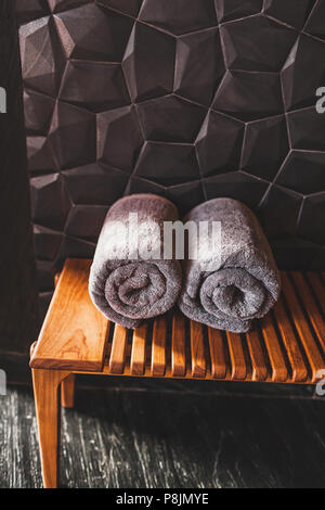 Two rolled grey towels on wooden bench in sauna. Spa in hotel Stock Photo