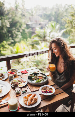 Beautiful girl with long black hair enjoying breakfast outdoor on wooden terrace Stock Photo