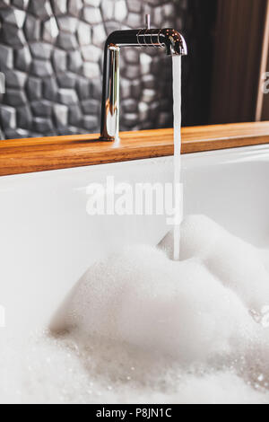 Water filling bath with foam. Modern style of bathroom with wooden edge and black walls Stock Photo