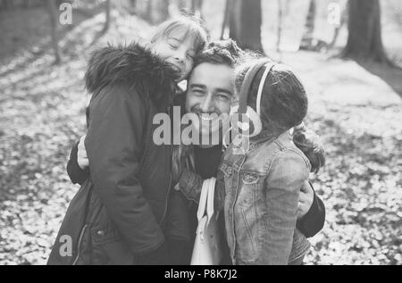 Dad and father on a family walk with his two daughters, hugging in the woods and laughing together. A black and white image. Stock Photo
