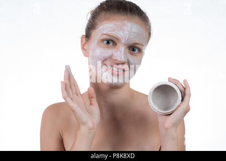 Two cosmetic mask of gray clay with scrub and cream on the face of a beautiful young girl and a jar with clay Stock Photo