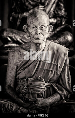 A portrait of an elderly male monk meditating in a temple in Thailand. Stock Photo