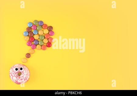Colorful glazed donuts with funny eyes on yellow background. Stock Photo