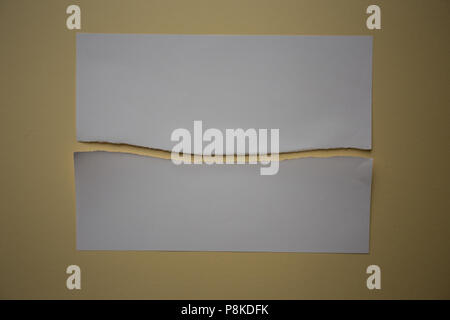 A piece of white paper ripped in half against a yellow background Stock Photo