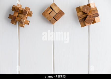 Three geometric interlocked wooden puzzles arranged in a neat line as a top border on white painted wood boards with copy space Stock Photo