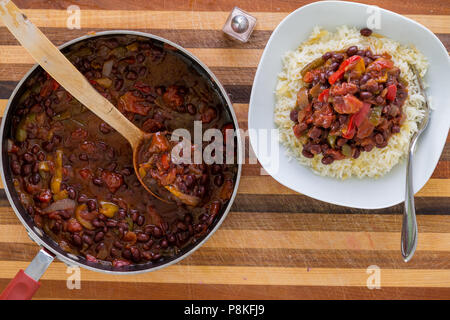 Pot of freshly cooked nutritious pinto beans and vegetables served onto a plate heaped with rice in an overhead view on a laminated decorative wooden  Stock Photo