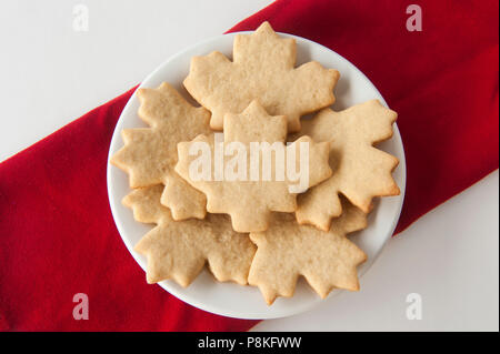 Plate of maple leaf shaped cookies on red and white background Stock Photo