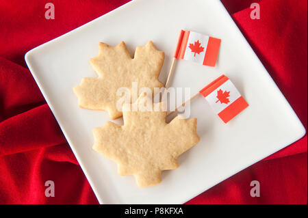 Two maple leaf shaped cookies on a plate with Canadian flags on red Stock Photo