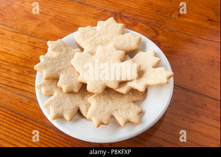Plate of plain leaf shaped cookies on a round white plate on a wooden table Stock Photo