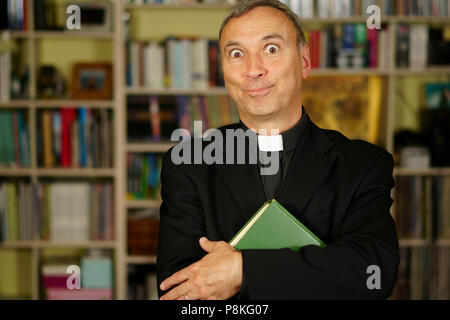 A good looking catholic priest is studying into his library. He looks at us with crazyness, interest, disapproval, judgement and apprehension. Stock Photo