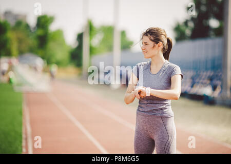 Sport and technology. beautiful young whiteskinned woman with ponytail at running stadium in front of workout uses a sporty smart clock on her arm to 