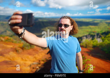 Young man taking a photo of himself or a selfie in Waimea Canyon on Kauai, Hawaii Stock Photo