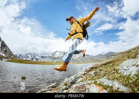Man hiker jumps from big rock at mountains area against lake Stock Photo