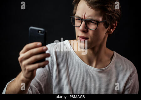close up side view portrait of student has an incomprehensible message in mobile phone. problems with smartpone. male with poor eyesight looking at th Stock Photo