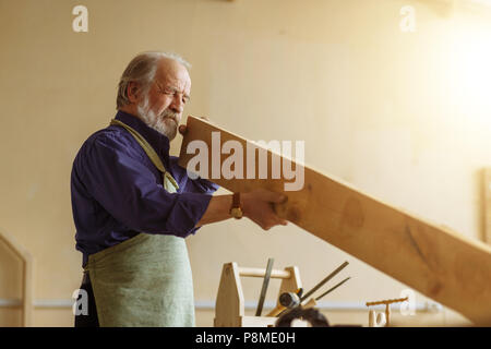 old handsome joiner is measuring the board in the workroom.craftsmanship concept Stock Photo