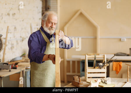 close up photo of working senior citizen with closed one eye holding plank on hands and choosing planks for furniture Stock Photo