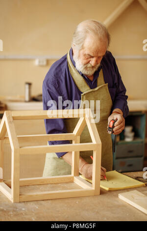 old successful carpenter writing sceleton plan in the notepad in the workshop Stock Photo