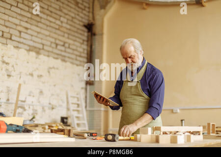close up side view portrait of old man with grey hair, moustache and beard working with tablet in the garage. copy space Stock Photo
