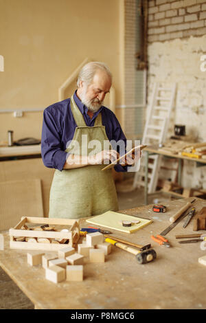 close up photo of old master making out an order from the Net. choose instruments for carpentry online. look at the screen. look for sponsor Stock Photo