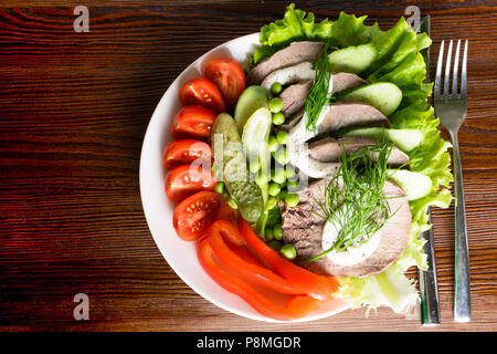 boiled tongue slices with vegetables tomatoes red pepper cucumber lettuce peas with mayonnaise on the wooden table Stock Photo