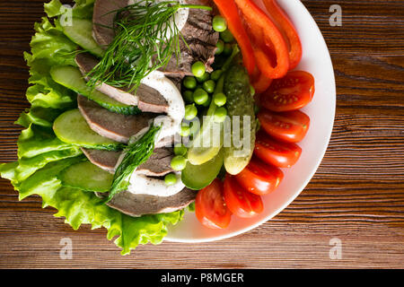 boiled tongue slices with vegetables tomatoes red pepper cucumber lettuce peas with mayonnaise on the wooden table Stock Photo