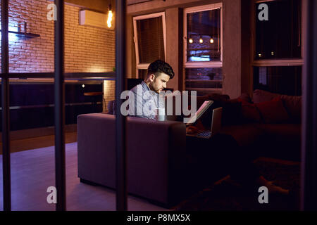 A man  freelancer with a laptop works in the evening. Stock Photo