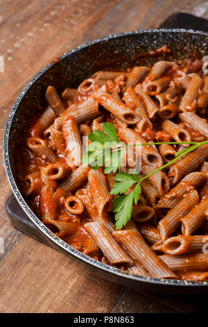 closeup of a frying pan with buckwheat penne rigate alla bolognese on a rustic wooden table Stock Photo