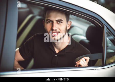 Young, handsome man fastens a seat belt, sitting in the back seat of the car. Stock Photo