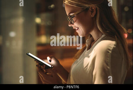 Side view of happy young woman looking at her smart phone and smiling. Businesswoman reading text message in office. Stock Photo