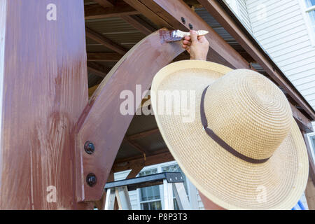 Unidentifiable man in a sunhat staining wooden beams on an outdoor gazebo near a house in a DIY concept Stock Photo