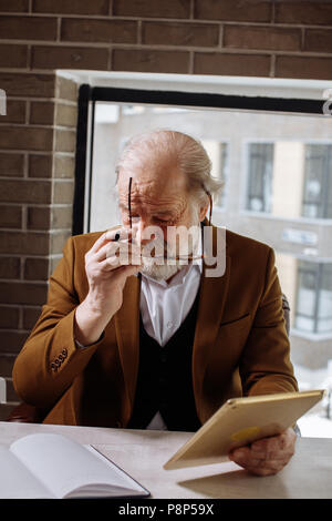 closeup vertical image of senior citizen putting on glasses while sitting on the armchair Stock Photo