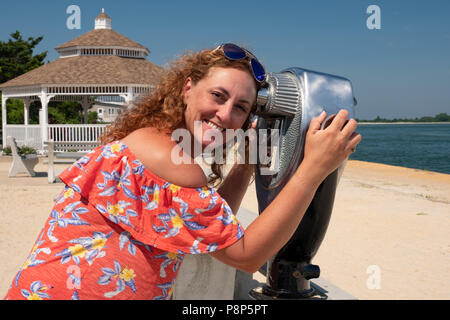 woman uses coin operated binocular to observe landscape, ocean, boats, beach scenes at the coast Stock Photo