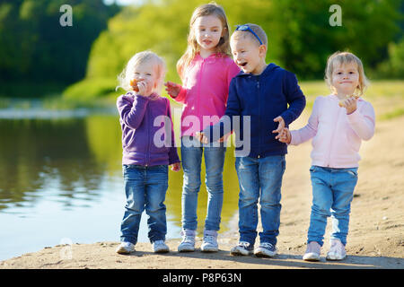 Three little sisters and their brother having fun, laughing and joking by a river at sunny autumn day Stock Photo