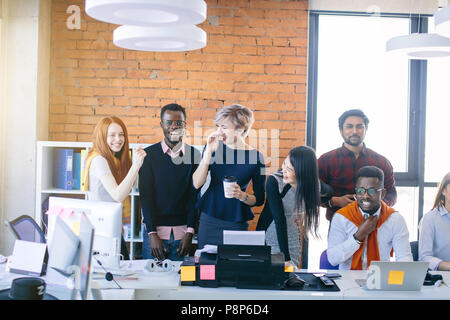 young multi ethnic people are laughing at work while their African partner feels bad. Afro man dislike his co-workers. feed up to the back teeth. Man  Stock Photo