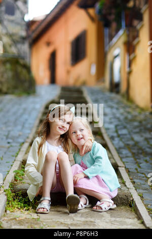 Two adorable little sisters laughing and hugging each other on warm and sunny summer day in italian town Stock Photo