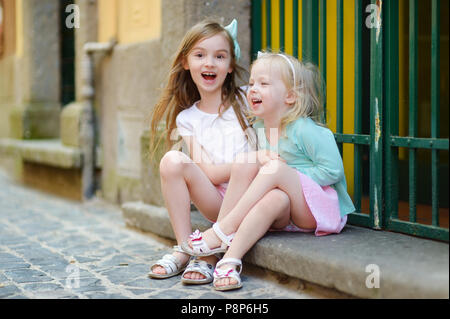 Two adorable little sisters laughing and hugging each other on warm and sunny summer day in italian town Stock Photo