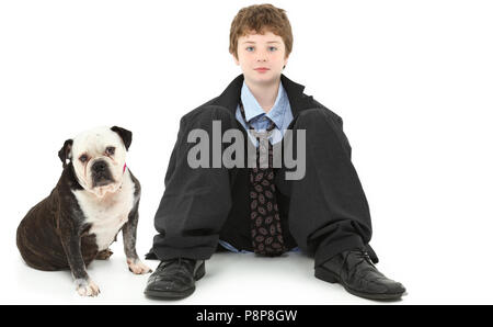 Handsome ten year old american boy in baggy suit sitting against white wall with Bulldog.