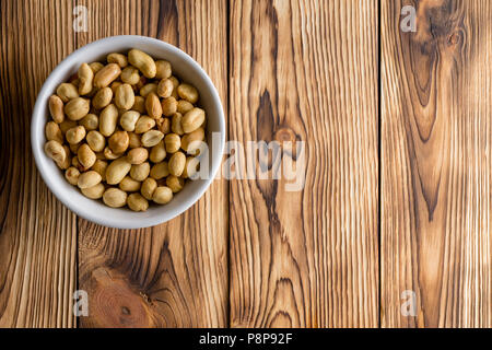 Generic white bowl full of fresh roasted shelled peanuts in the corner on a rustic wooden table with copy space viewed from above Stock Photo