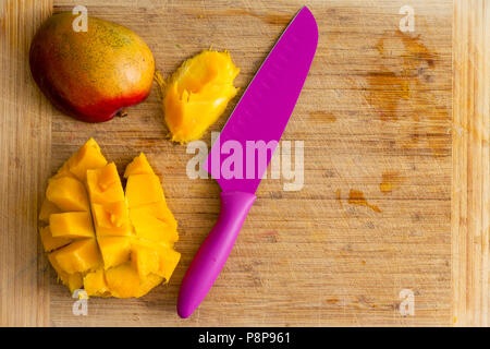 Sliced mango hedgehog with pink kitchen knife and pip on a bamboo cutting board with copy space Stock Photo
